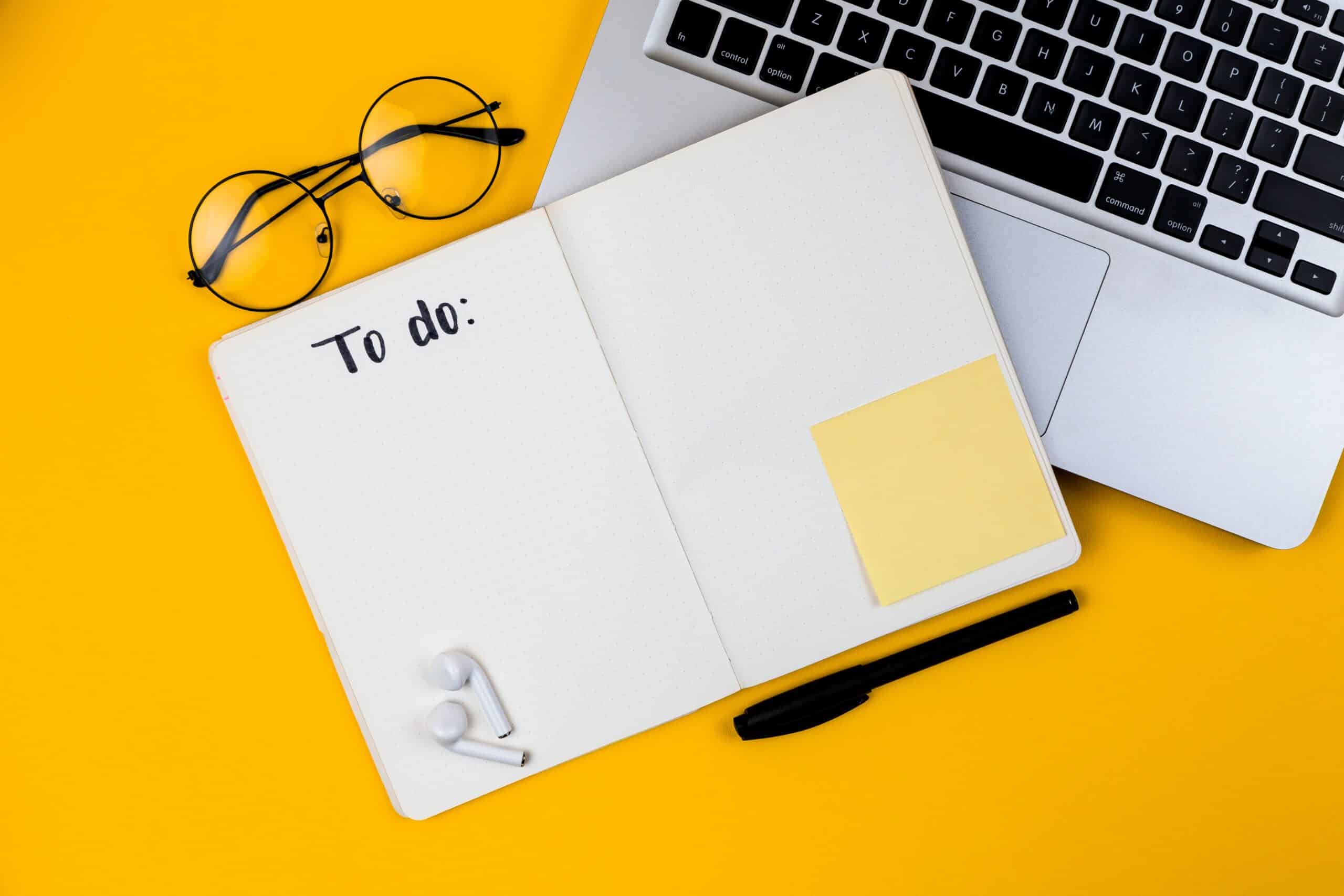 open notebook that says, "to do" on a table with glasses and a computer